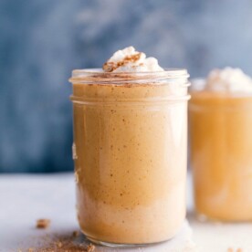 A cup filled with a creamy pumpkin protein shake, topped with a swirl of whipped cream.