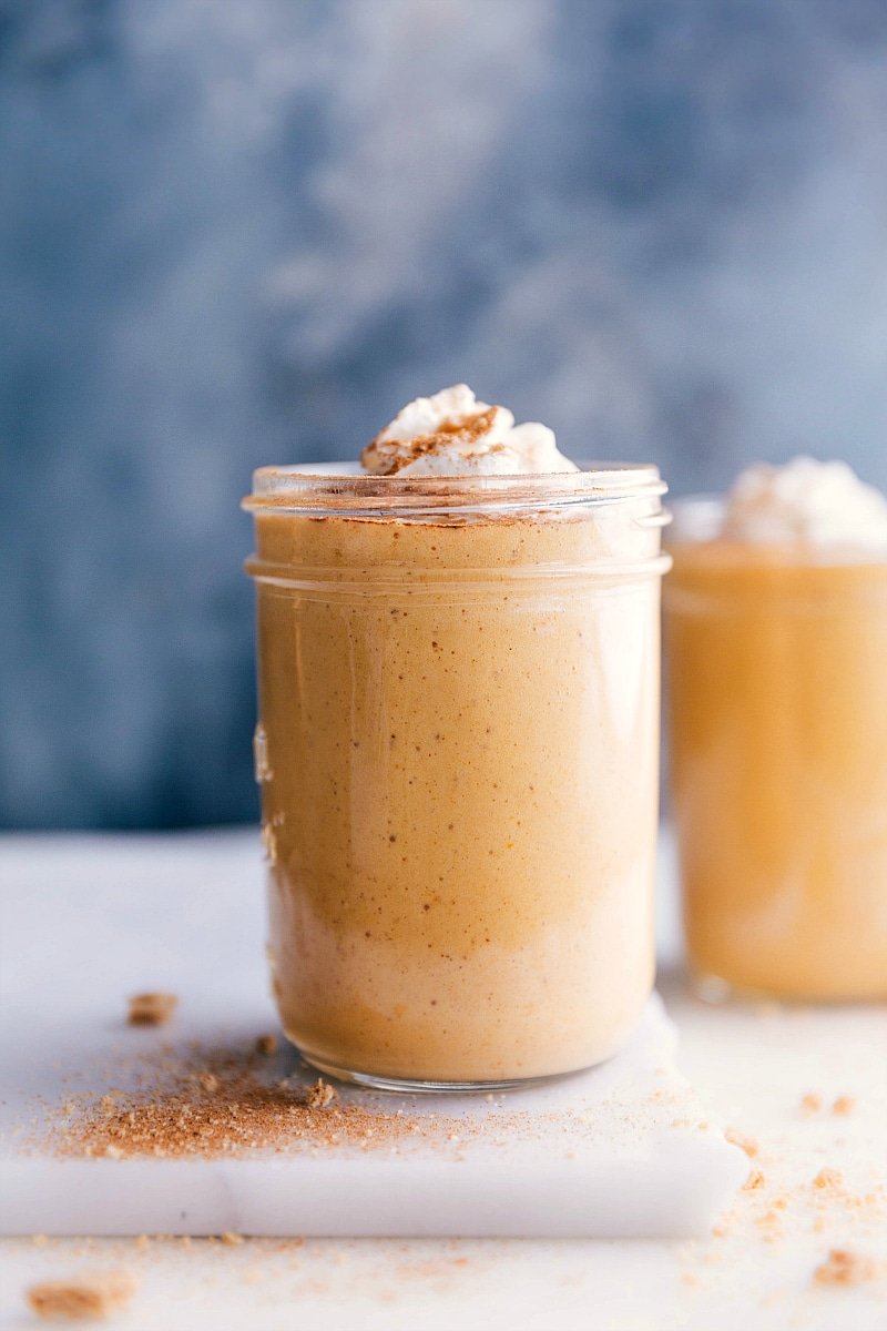 A cup filled with a creamy pumpkin protein shake, topped with a swirl of whipped cream.