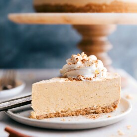 A tempting slice of no-bake pumpkin cheesecake with the whole cheesecake in the background, ready to be savored.