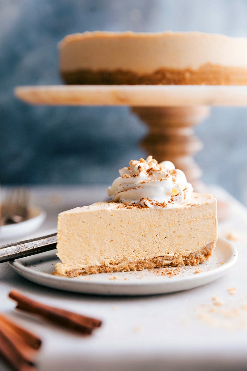 Image of a slice of No-Bake Pumpkin Cheesecake with the whole cheesecake in the background.