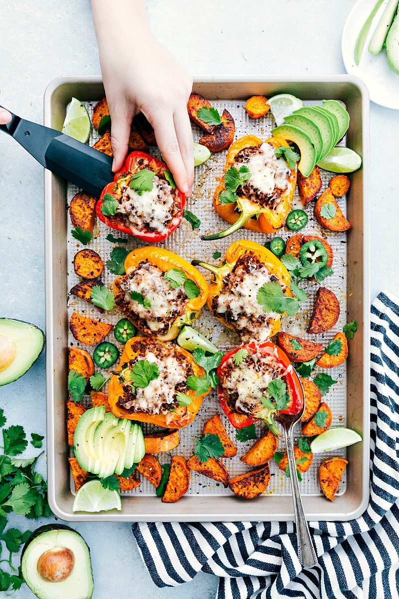 Sheet pan Mexican Taco Stuffed Sweet Peppers with Sweet potatoes on the edges garnished with lime, cilantro, and avocado.