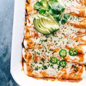 Vegetarian enchiladas fresh out of the oven, in the pan, garnished with avocado and cilantro.