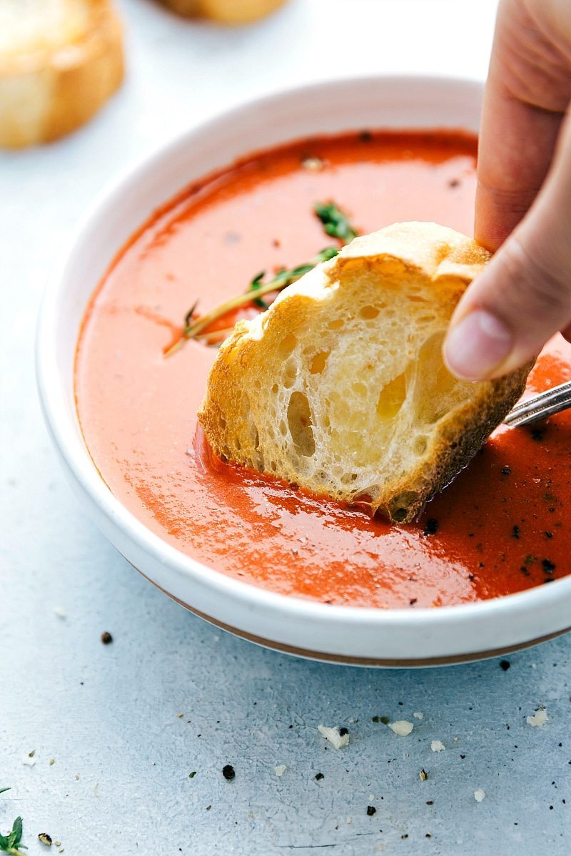 Tomato basil soup in a bowl with bread being dipped in.