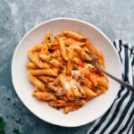 Warm and delicious red and white pasta in a bowl, complete with a fork and topped with freshly shredded cheese.