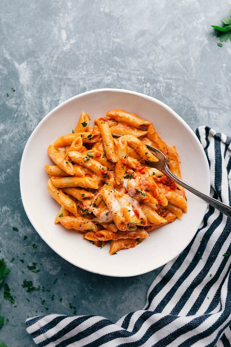 Warm and delicious red and white pasta in a bowl, complete with a fork and topped with freshly shredded cheese.