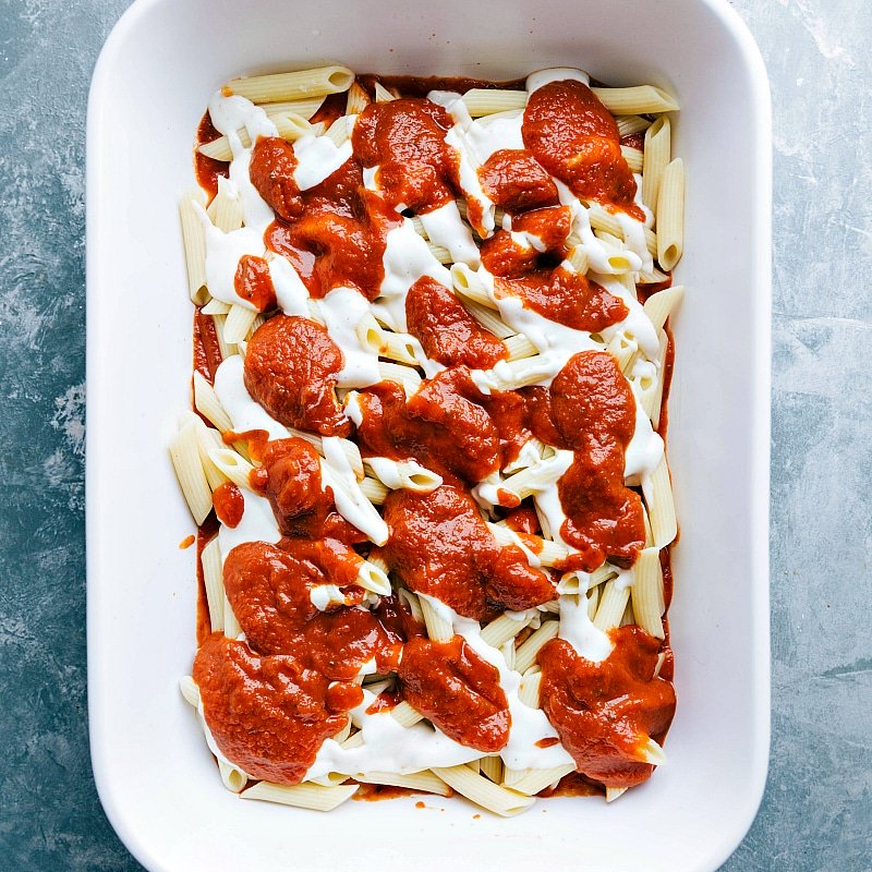 Marinara sauce being layered on top of alfredo sauce in a pasta dish, creating a rich flavor combination.