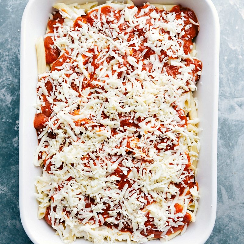 Mozzarella cheese being sprinkled on top of the red and white sauce pasta casserole, ready for baking.