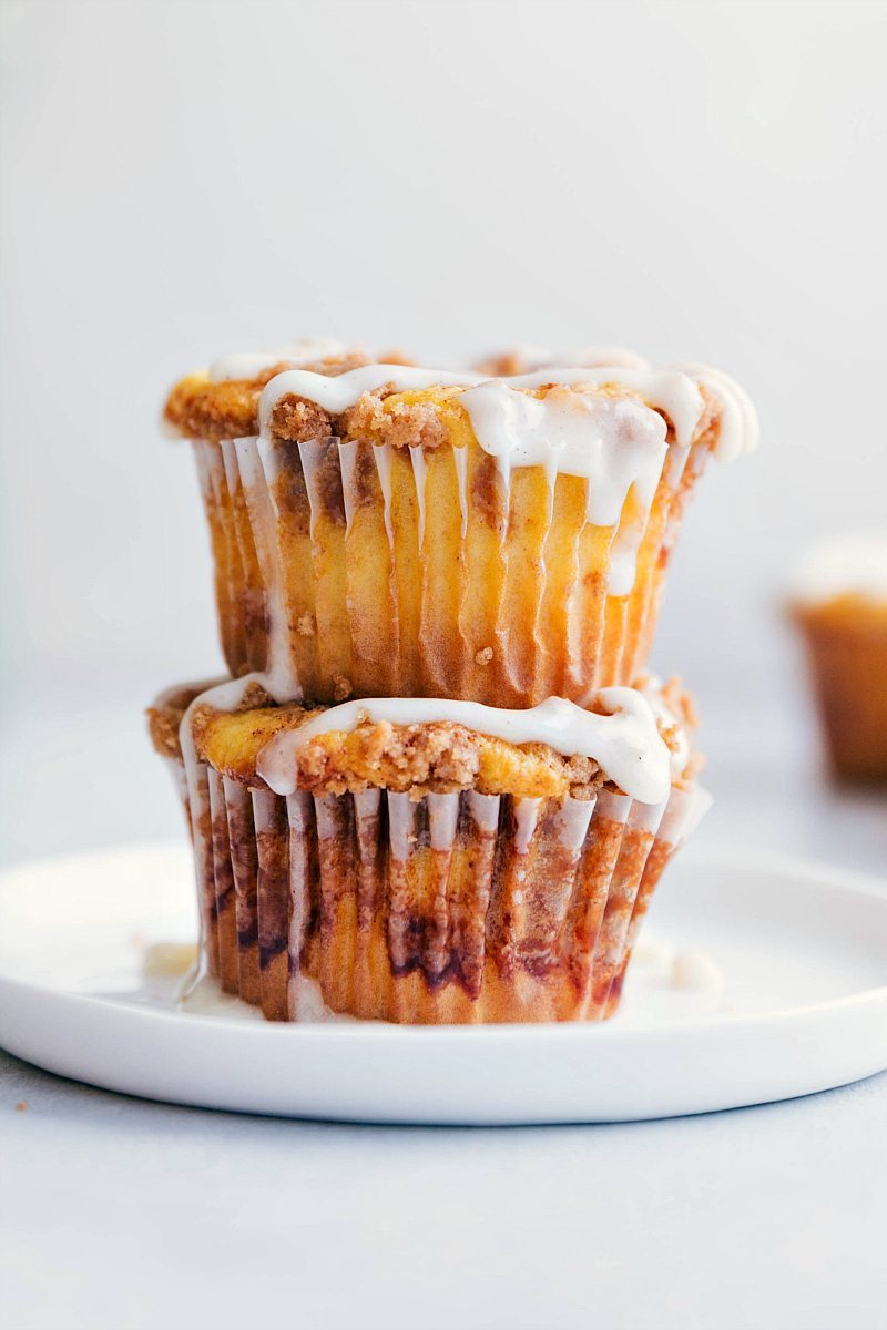 Two cinnamon roll cupcakes stacked on one another on a white plate. 