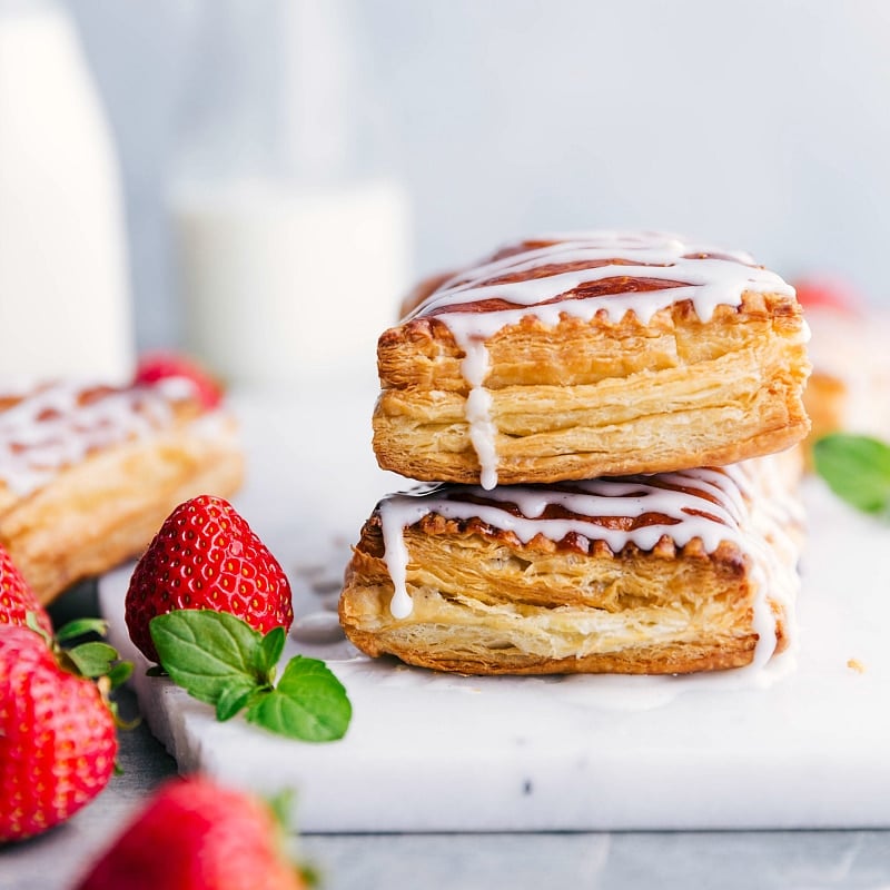 Two stacked Toaster Strudels with dripping icing, accompanied by fresh strawberries on the side.