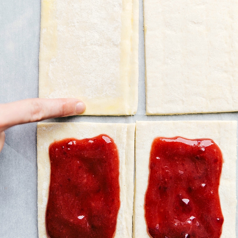 Egg wash being brushed onto the edges of puff pastry to seal the layers.