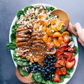 Chicken spinach salad on a large platter, elegantly dressed and garnished with fresh fruit and nuts.