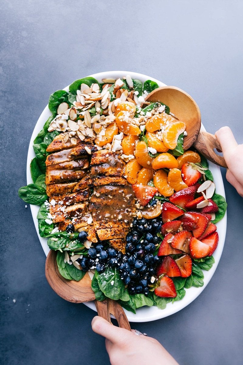 Chicken spinach salad on a large platter, elegantly dressed and garnished with fresh fruit and nuts.