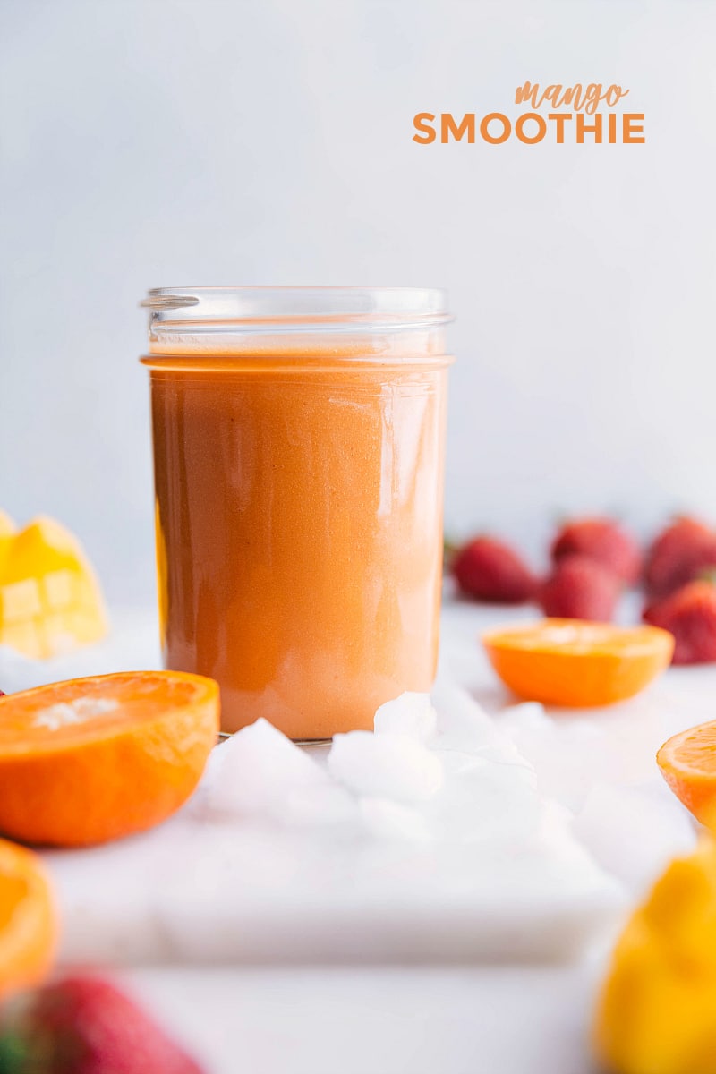 Image of the prepared mango smoothie with fruit and ice around it.