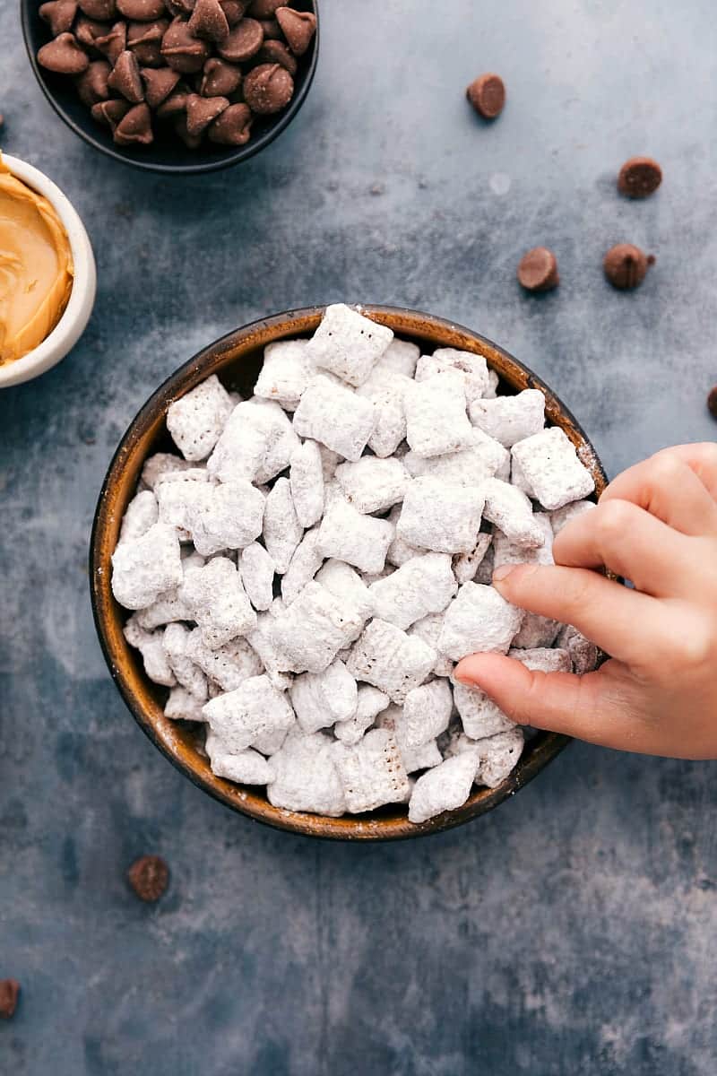 Overhead photo of a bowl filled with Muddy Buddies and a toddler hand grabbing one out.