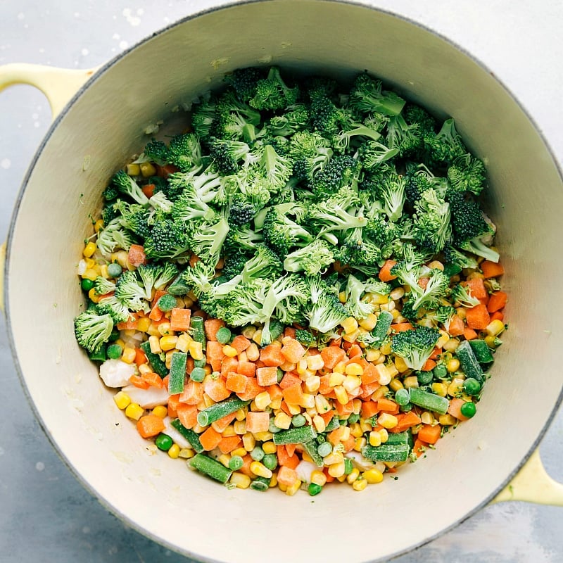 Frozen vegetables and fresh broccoli being added to the sauce pan.