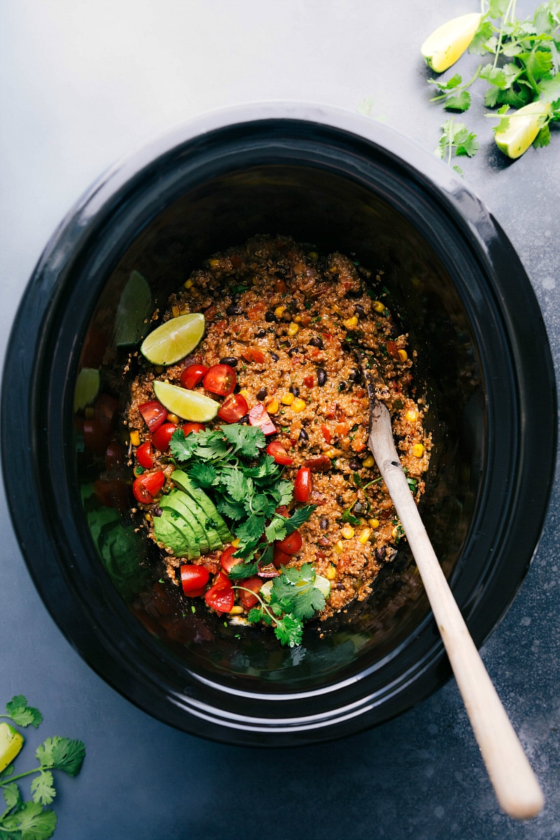 Tex mex quinoa in the crockpot with a spoon and fresh toppings ready to be enjoyed.