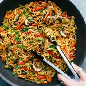 Chow Mein with tongs, ready to be served, filled with veggies and coated in a delicious sauce.