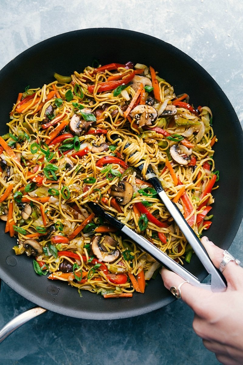 Chow Mein with tongs, ready to be served, filled with veggies and coated in a delicious sauce.