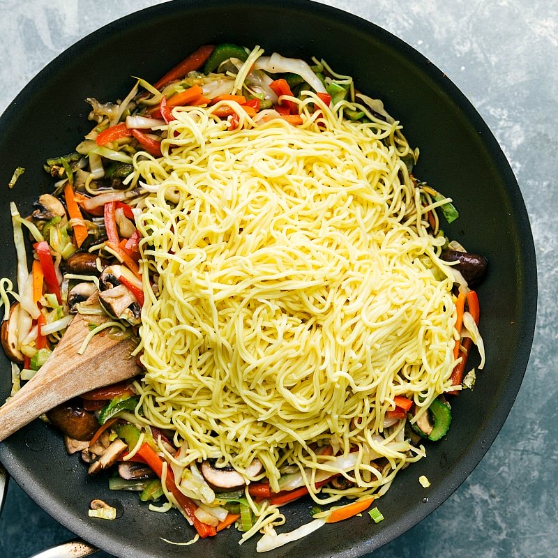 Adding noodles to the skillet filled with vegetables.