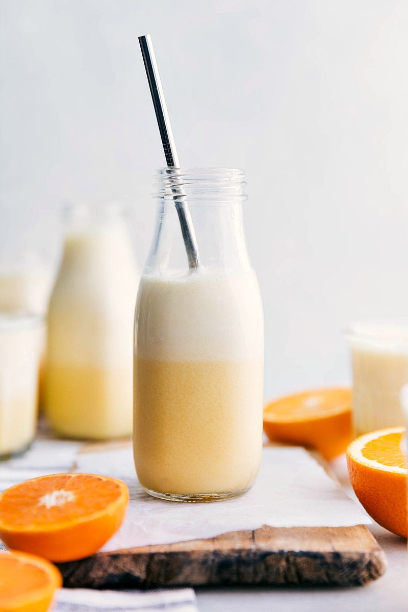 Ready-to-drink Orange Julius with a straw in it and cut oranges around it.