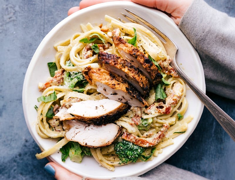 Bowl of creamy chicken pesto pasta with fresh rotisserie chicken on top, ready to be enjoyed.