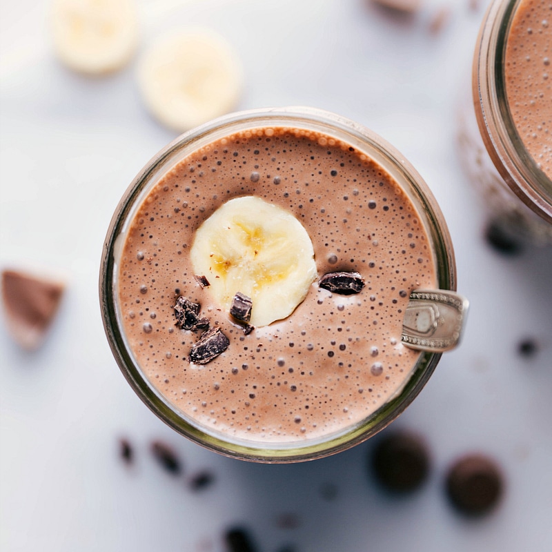 Overhead image of Peanut Butter Protein Shake showing the shake with a banana slice and chocolate chips on top with a spoon.