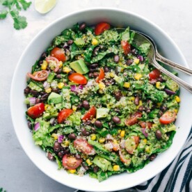 A bowl filled with a flavorful and healthy southwest quinoa salad, accompanied by two serving spoons on the side.