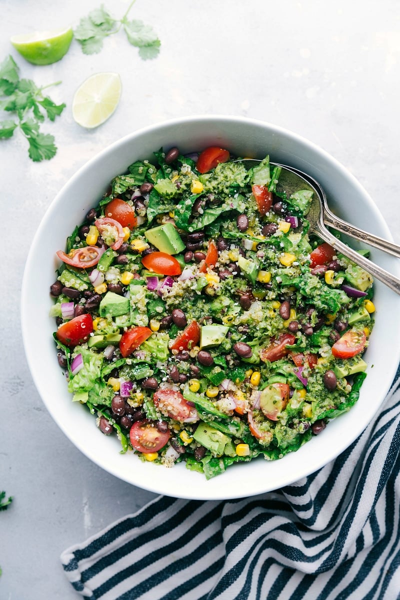 A bowl filled with a flavorful and healthy southwest quinoa salad, accompanied by two serving spoons on the side.