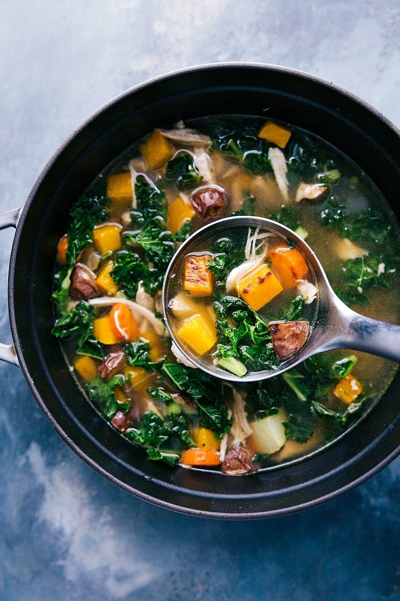 Chicken vegetable soup in the pot, with a ladle scooping up a steaming portion.