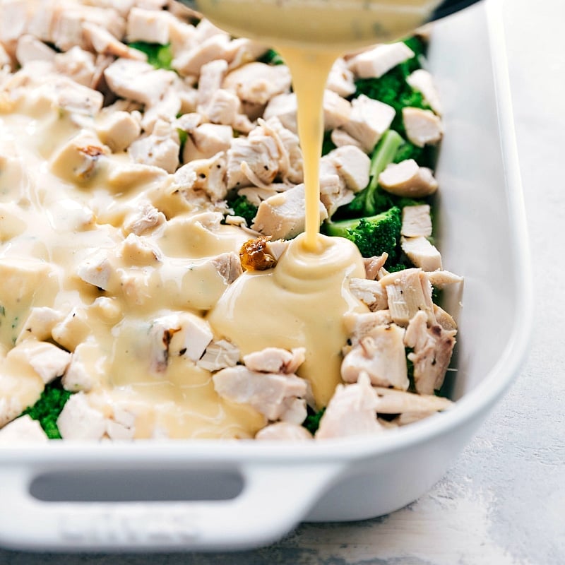 Pouring creamy, cheesy sauce over the dish in preparation for cooking.