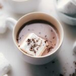 Homemade marshmallows floating in a cup of hot chocolate, topped with chocolate shavings.
