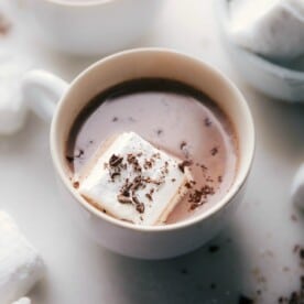 Homemade marshmallows floating in a cup of hot chocolate, topped with chocolate shavings.