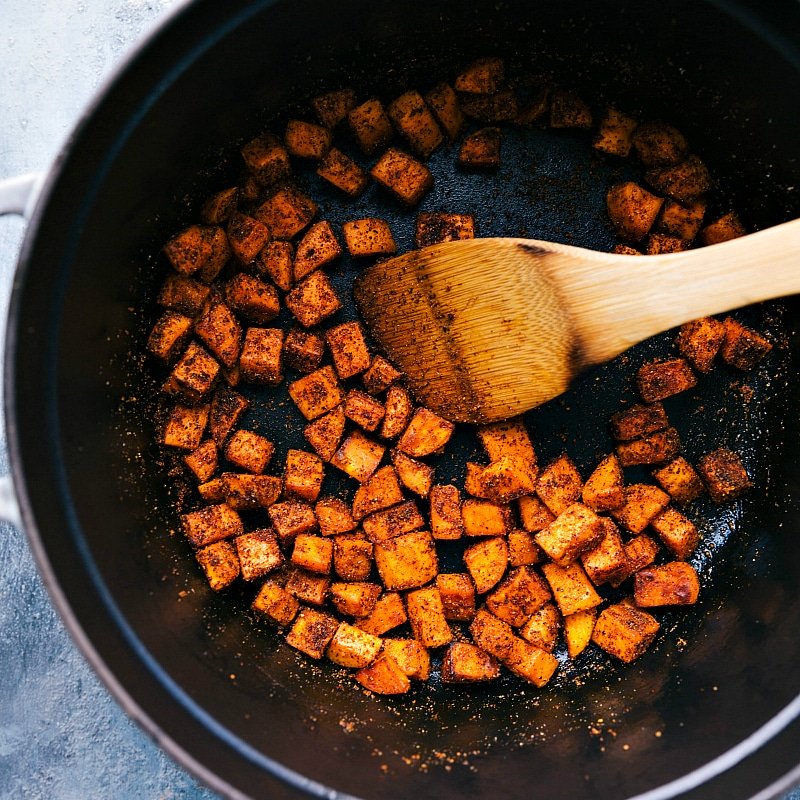 Sweet potatoes being sautéed with seasonings in a pan, infusing them with flavor.