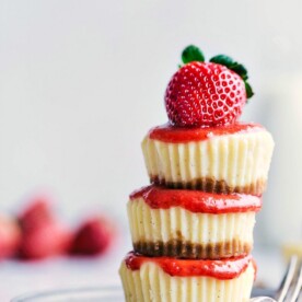 Three mini cheesecakes beautifully stacked, topped with a ripe strawberry.