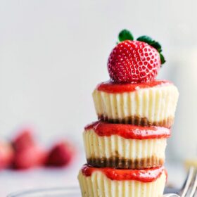 Three mini cheesecakes beautifully stacked, topped with a ripe strawberry.