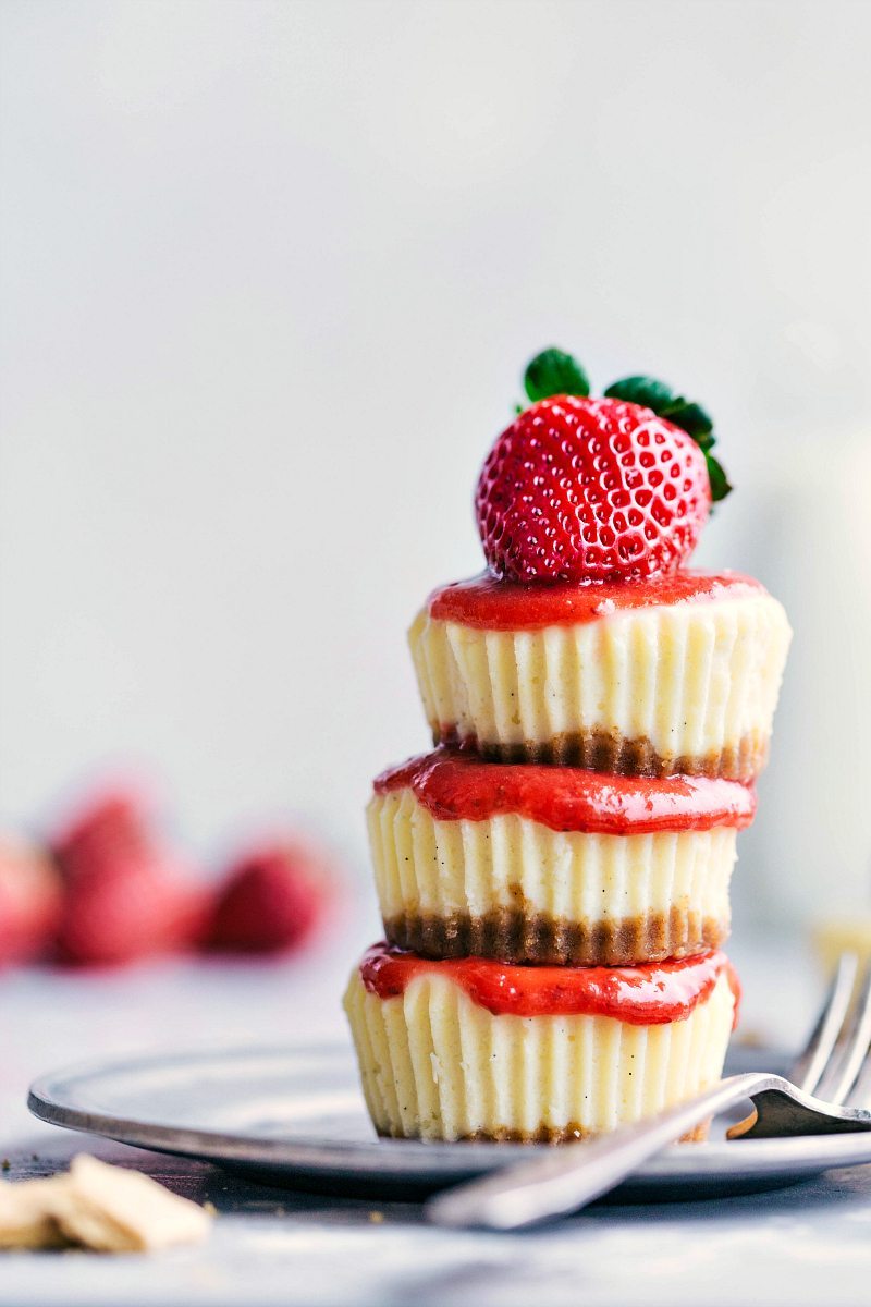 Three mini cheesecakes beautifully stacked, topped with a ripe strawberry.