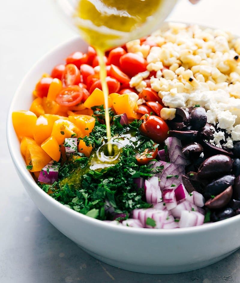 Image of the dressing being poured over the ingredients for this Orzo Pasta Salad with feta.