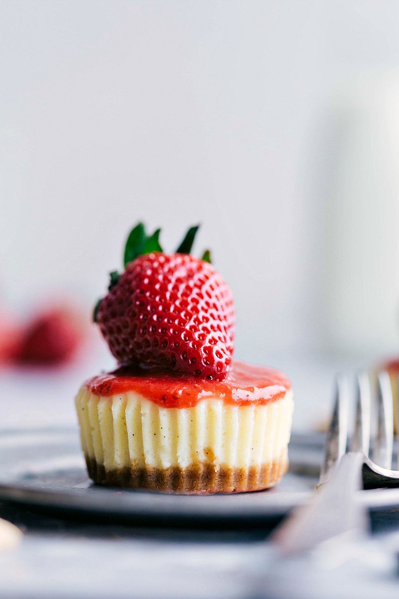 One single Mini Cheesecake with strawberry sauce and a whole strawberry on top.