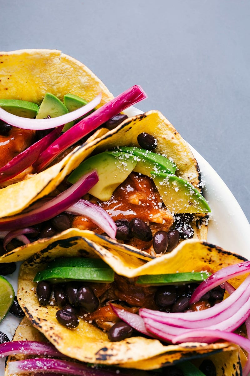 Chipotle chicken tacos on a platter, topped with fresh vegetables and beans.