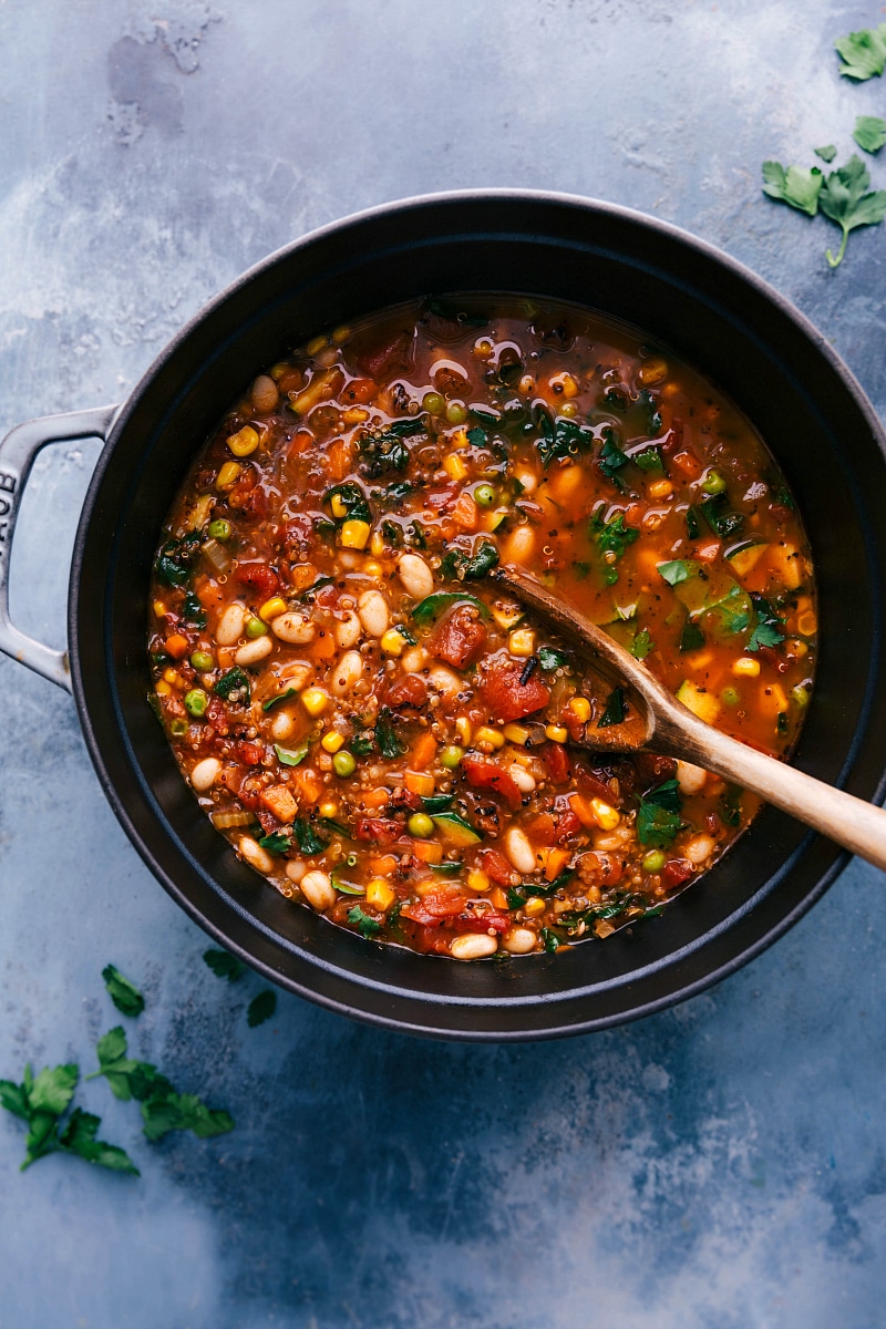 Pot of finished meal, brimming with vegetables, with a big wooden spoon.