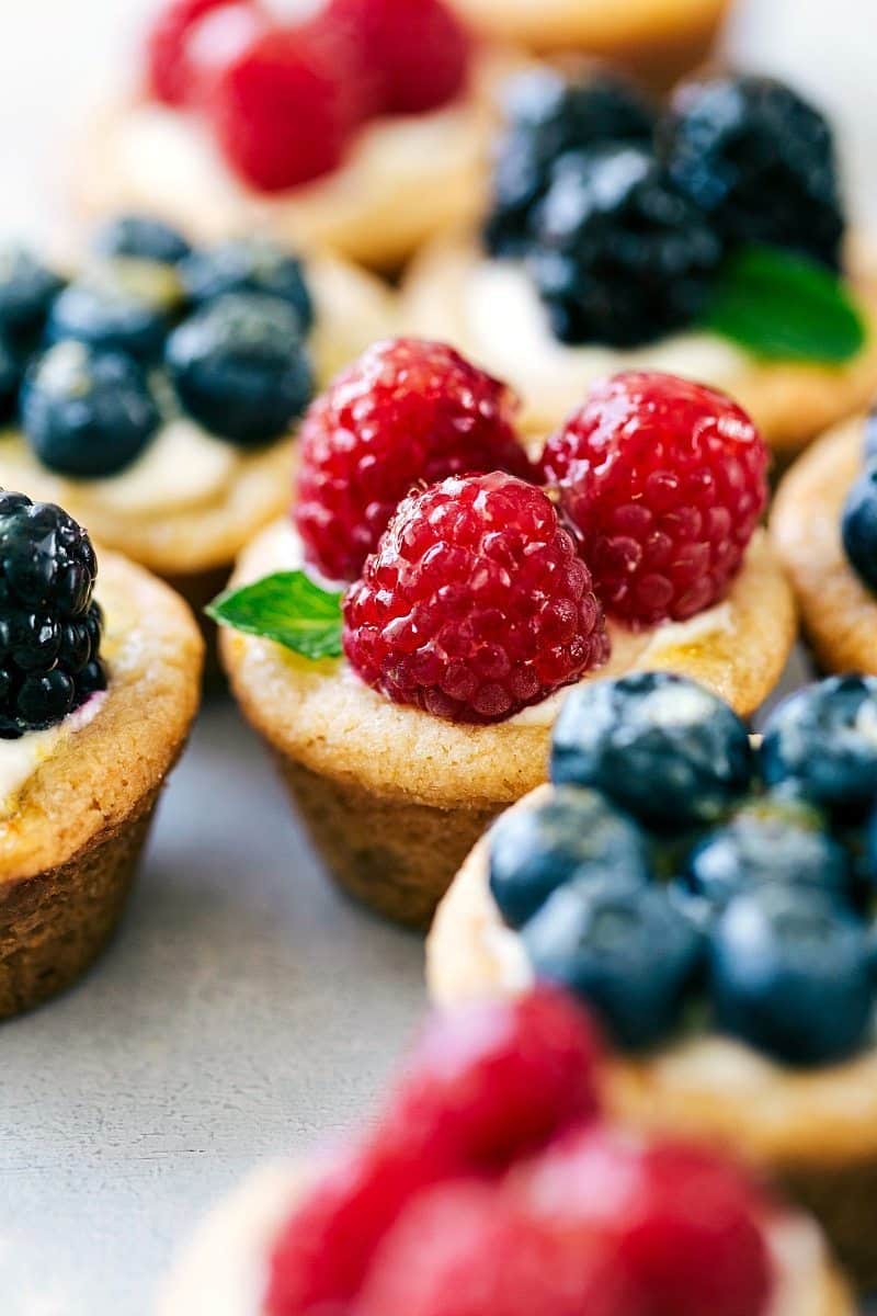 Mini fruit tarts topped with raspberries, blueberries, blackberries, and fresh mint.