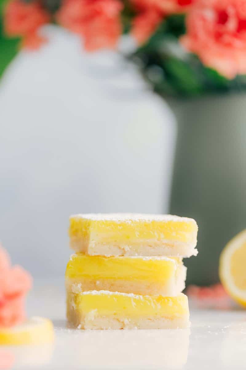 These Lemon Bars start with a simple shortbread crust and are topped with a tangy, sweet, and creamy lemon topping. Sprinkle on some powdered sugar for the perfect finishing touch! Recipe via ChelseasMessyApron #dessert #best #quick #easy #simple #treat #summerdessert #summer #lemon #bars Up-close shot of three Lemon Bars stacked on top of each other
