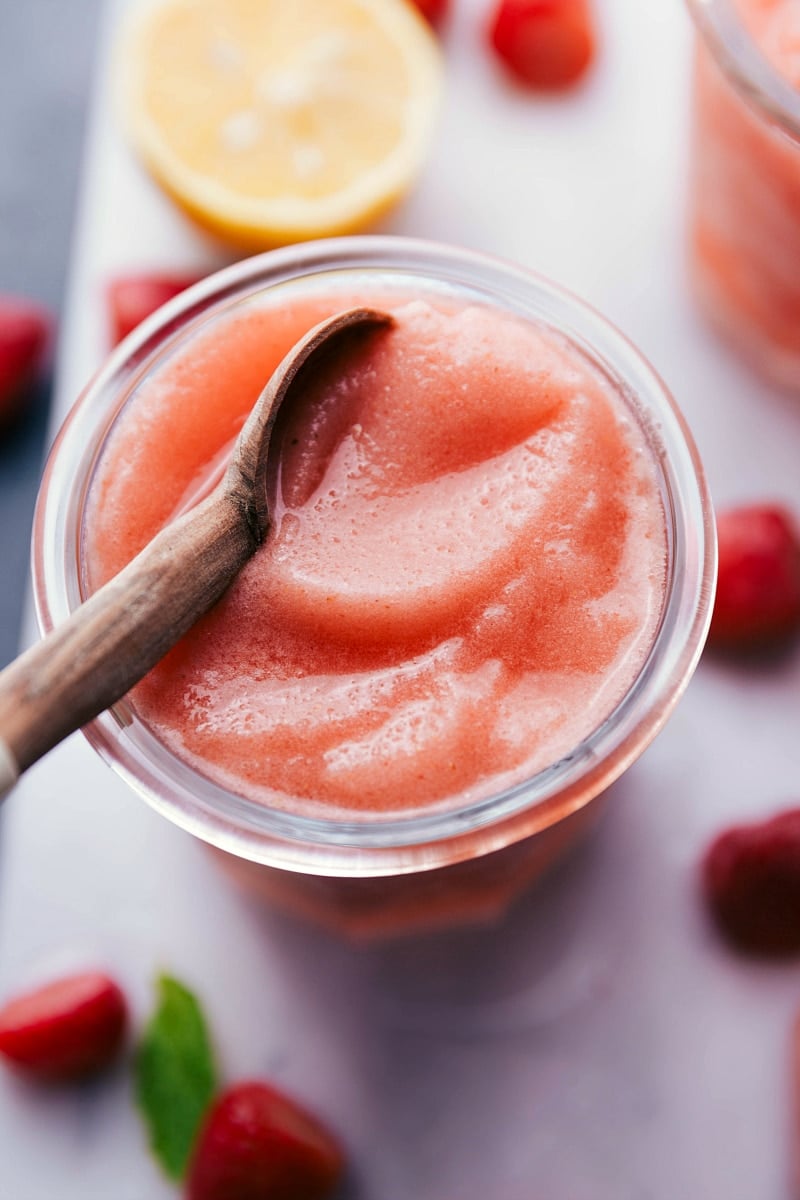 Chilled lemon berry slush with a spoon, strawberries, and mint on the side.