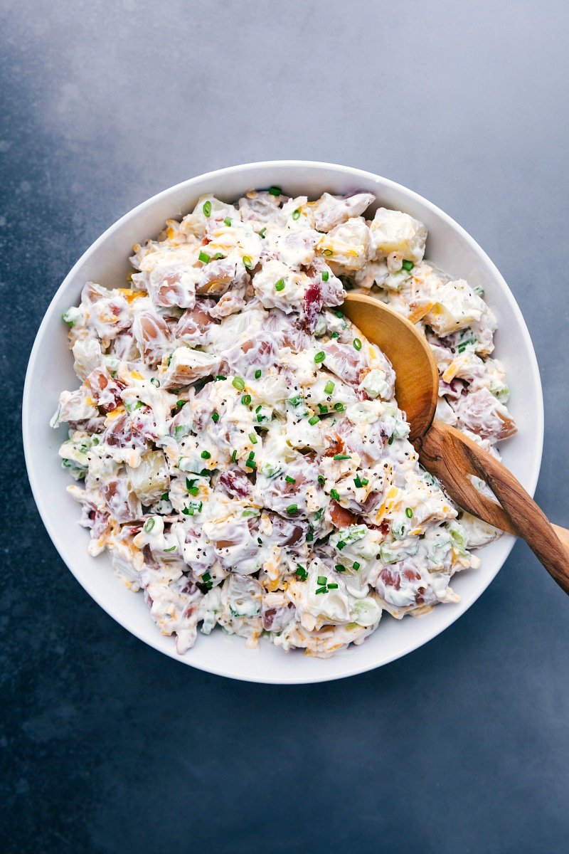 Overhead image of a large bowl Ranch Potato Salad with a wooden spoon in it.