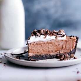 A decadent slice of nutella pie, crowned with whipped cream and chocolate shavings, on a plate with a spoon, inviting a bite.