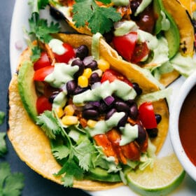 Finished BBQ chicken tacos topped with vegetables, beans, cilantro, and creamy dressing, ready to serve.