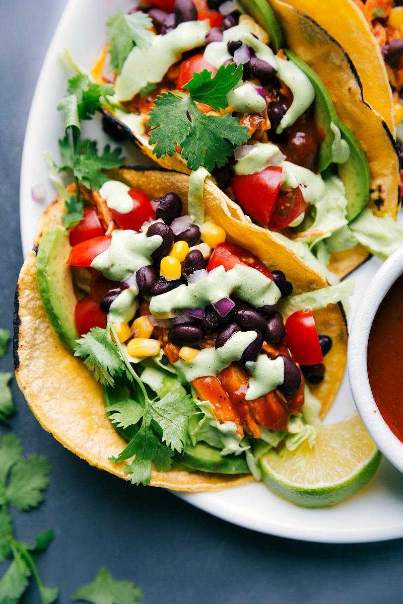 Finished BBQ chicken tacos topped with vegetables, beans, cilantro, and creamy dressing, ready to serve.