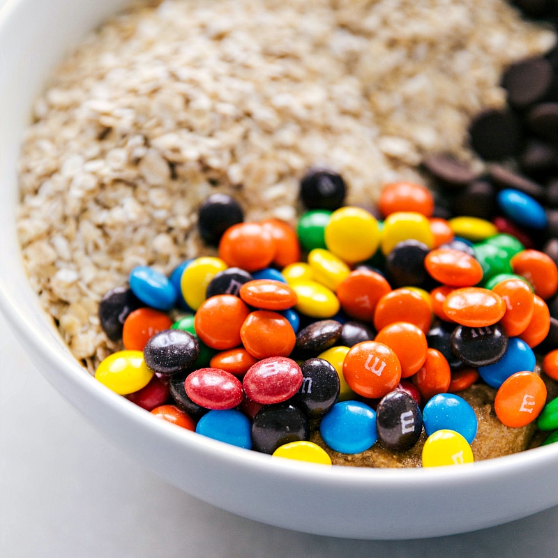 Flourless Monster Cookies made with a few healthier swaps Oats, chocolate chips, and M&M's being added to the bowl.