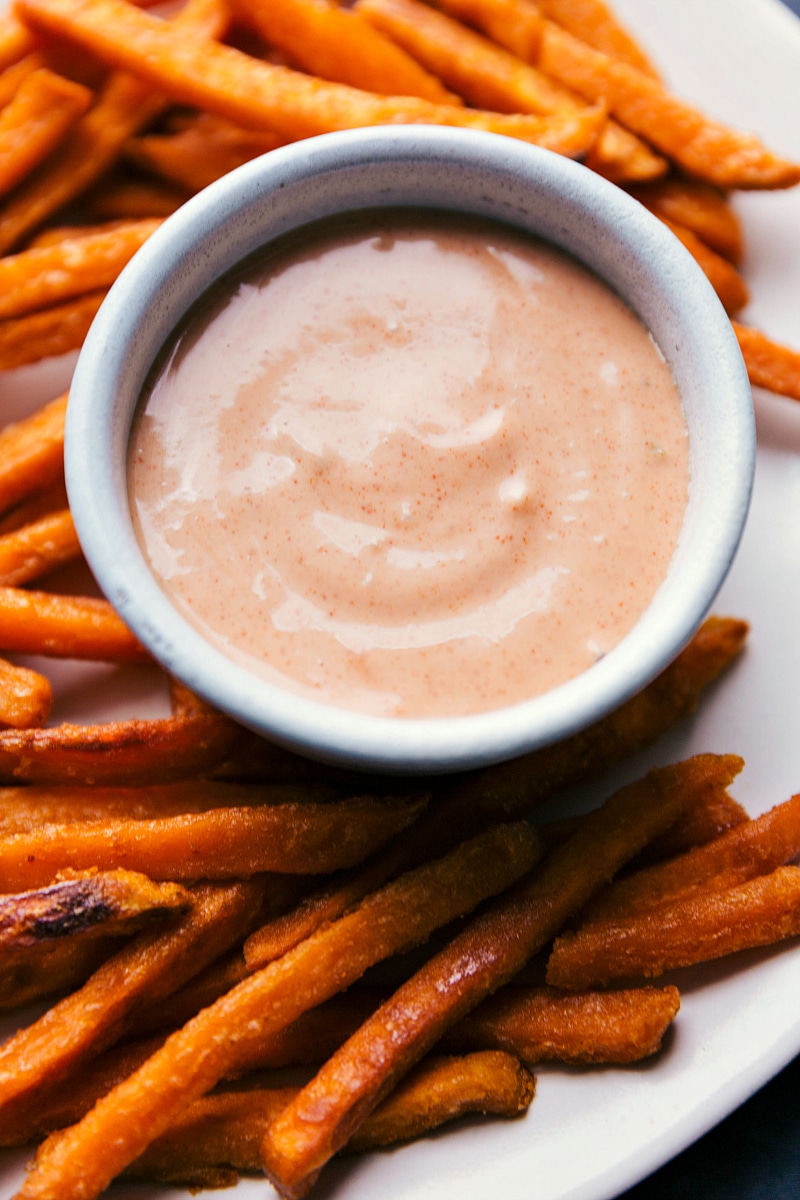 Creamy condiment in a small bowl with crispy sweet potatoes on the side.