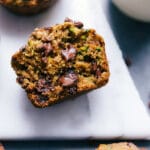 Gluten free zucchini muffins, with one split open to show the insides revealing the fluffy muffin, zucchini, and melted chocolate chips.